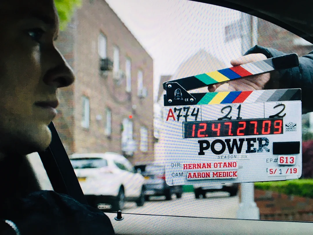 actor sitting in car with clapboard in background